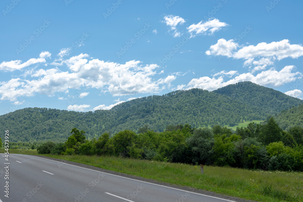 highway road and mountain peaks on the background of a blue sky with clouds