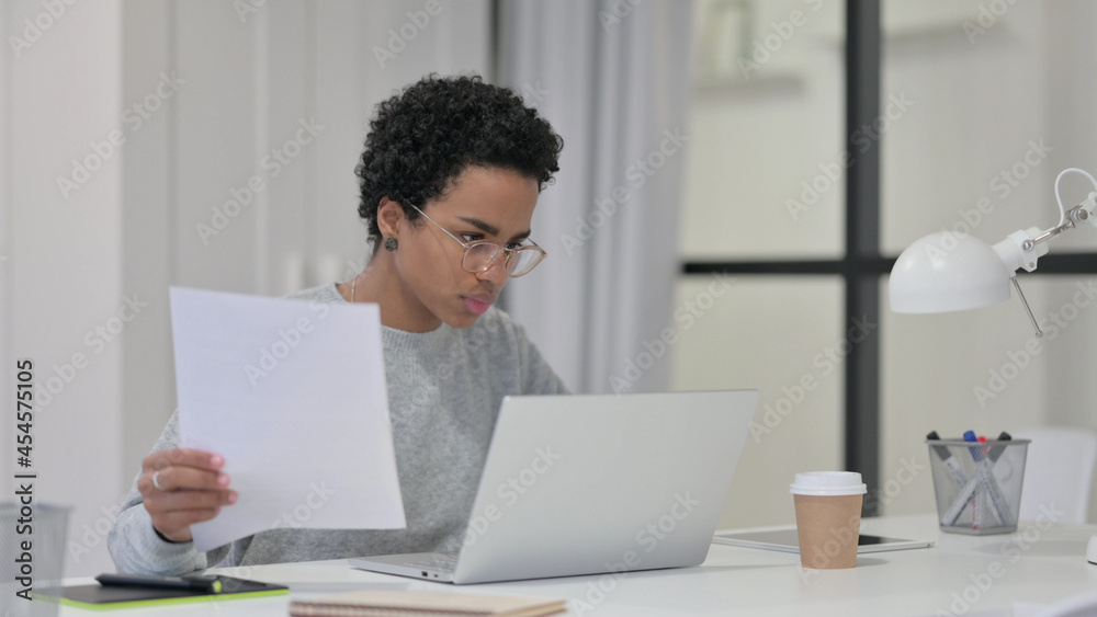 African Woman Reading Documents while using Laptop African Woman Reading Documents while using Laptop