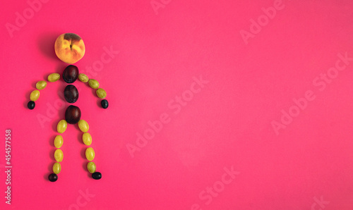A human figure made of grape grains, plums and peach on pastel red background. Minimalistic creative funny autumn concept, flat lay composition
