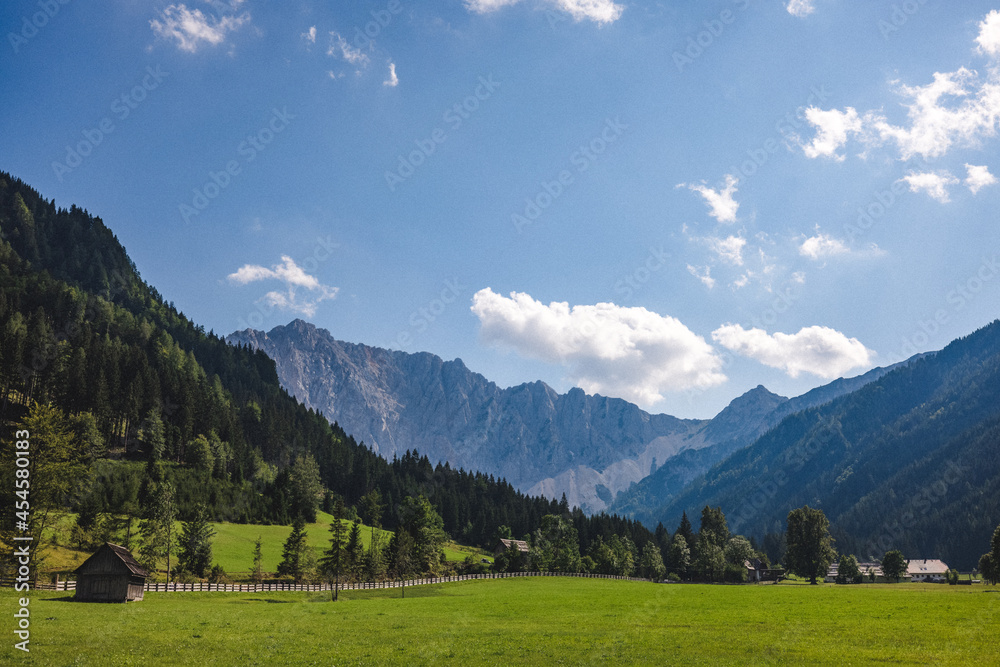 Grüne Wiese mit kleinem Holzhaus vor Alpenpanorama bei blauem Himmel