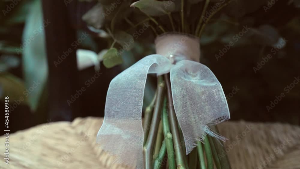 Detalle en forma de lazo de un ramo de novia sobre una silla de mimbré