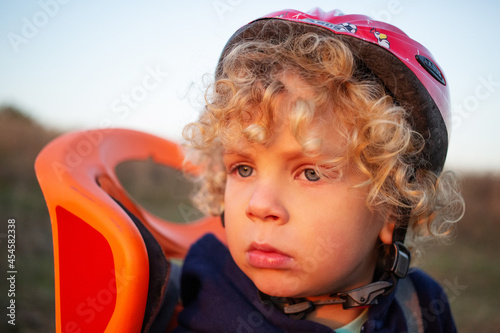 White curly boy in a helmet in a bicycle seat