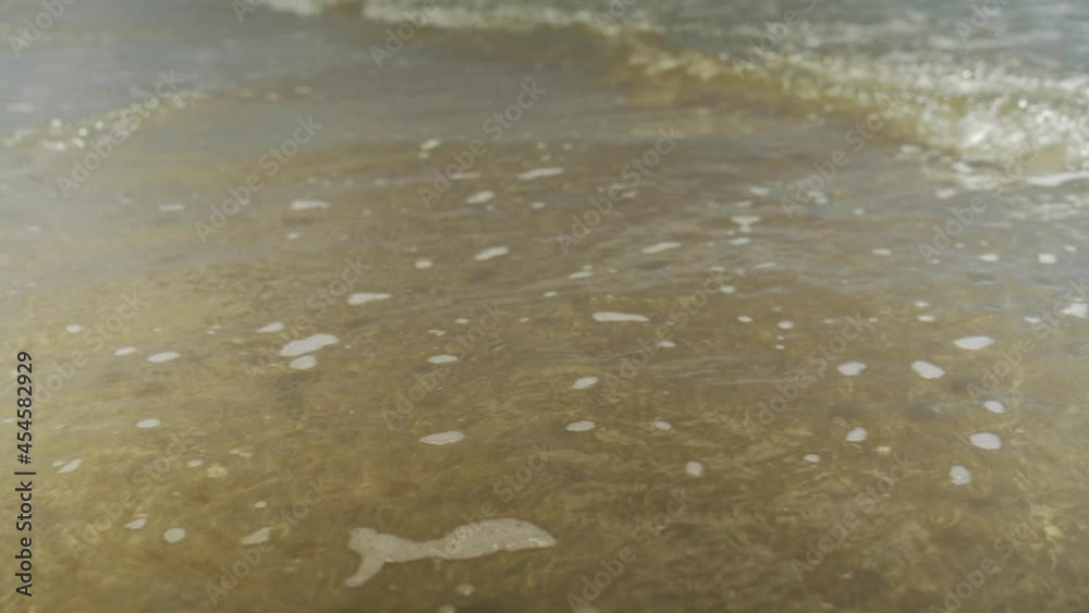 Movimientos de la marea en la orilla de la playa, pequeñas olas creando una capa de espumA