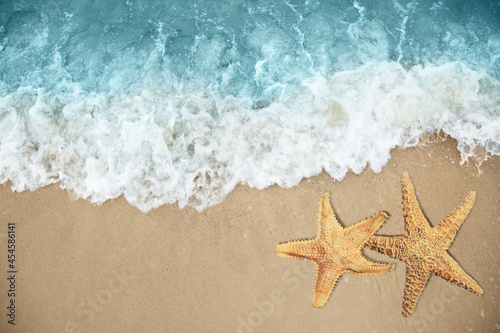 Beautiful waves and sea stars on sandy beach, top view