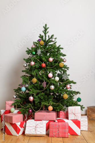 Wrapped boxes with gifts under a Christmas tree in a light room.