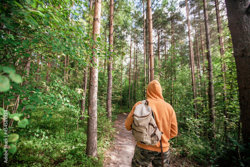 Man hiking with backpack in green forest. Back view