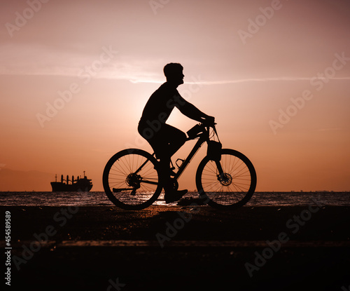 Silhouette of man riding bicycle along the coastal road during the sunset.