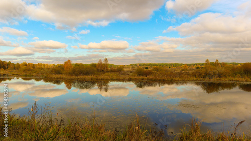 Beautiful landscape of autumn nature with a river field, forest and clouds. © Valery