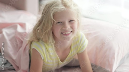 Portrait handsome cute little blonde girl having fun in bed in the morning. Adorable kid spinning, laughing, lying upside down.