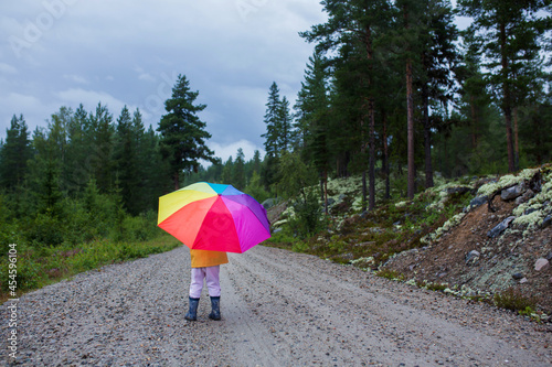 Cute toddler child with colorful umbrella  playing in the forest on a rainy day