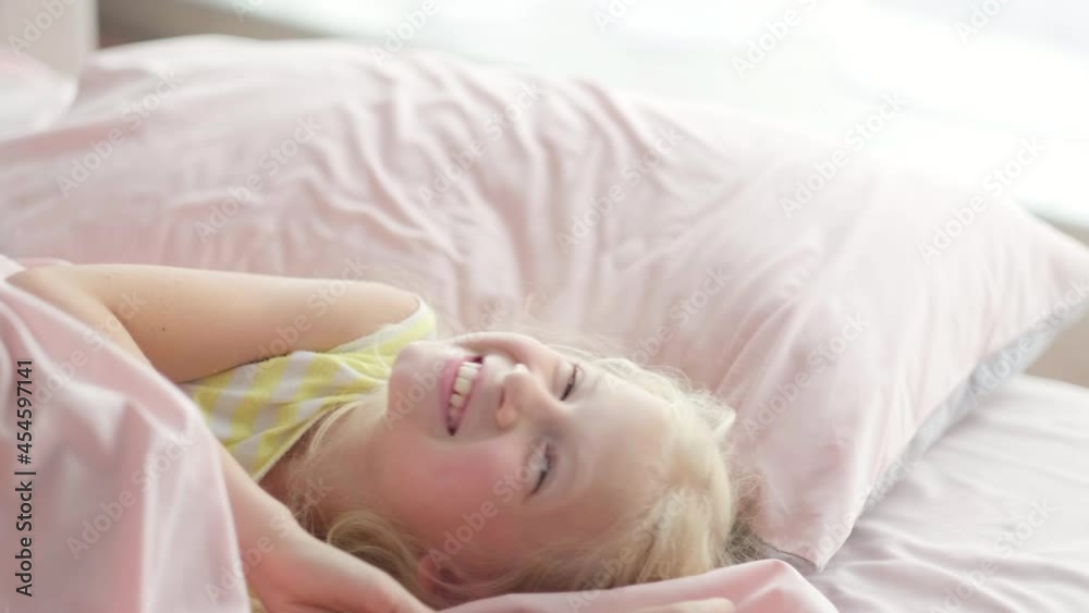 Portrait handsome cute little blonde girl having fun in bed in the morning. Adorable kid spinning, laughing, lying upside down. Portrait handsome cute little blonde girl having fun in bed in the morning. Adorable kid spinning, laughing, lying upside down.