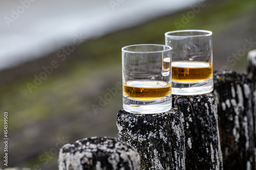 Tasting of dram single malt scotch whisky on seashore in Scotland, old wooden pole with whisky glass