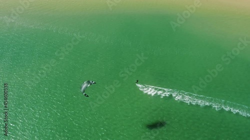 Overhead shot of kitesurfer gliding in the ocean on board with parachute at Alvor beach, Portugal, Europe. Drone flying over sportsman making trick during kitesurfing in summer time, 4k footage