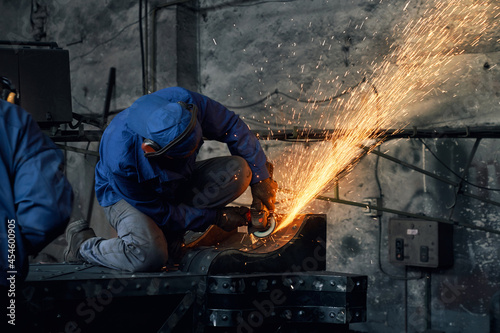 Qualified craftsman dressed in protective clothing welding metal frame on industrial factory. Sparks around. Manual working process.  © serhiibobyk
