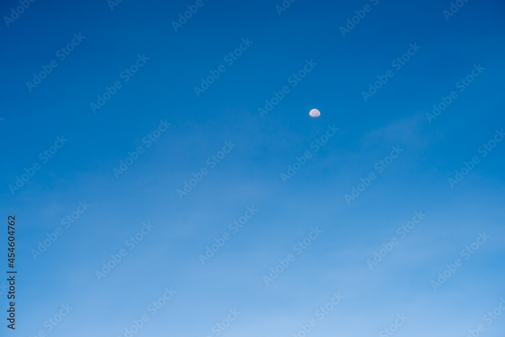 Half moon on blue bright sky background and clear clouds on daytime Half moon on blue bright sky background and clear clouds on daytime