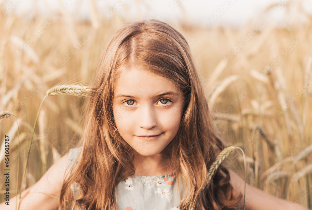 Beautiful little girl blonde with long hair walking through a wheat field