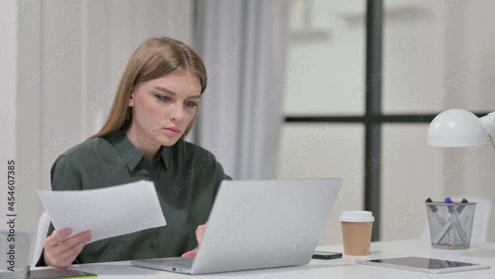 Young Woman Reading Documents while working on Laptop Young Woman Reading Documents while working on Laptop