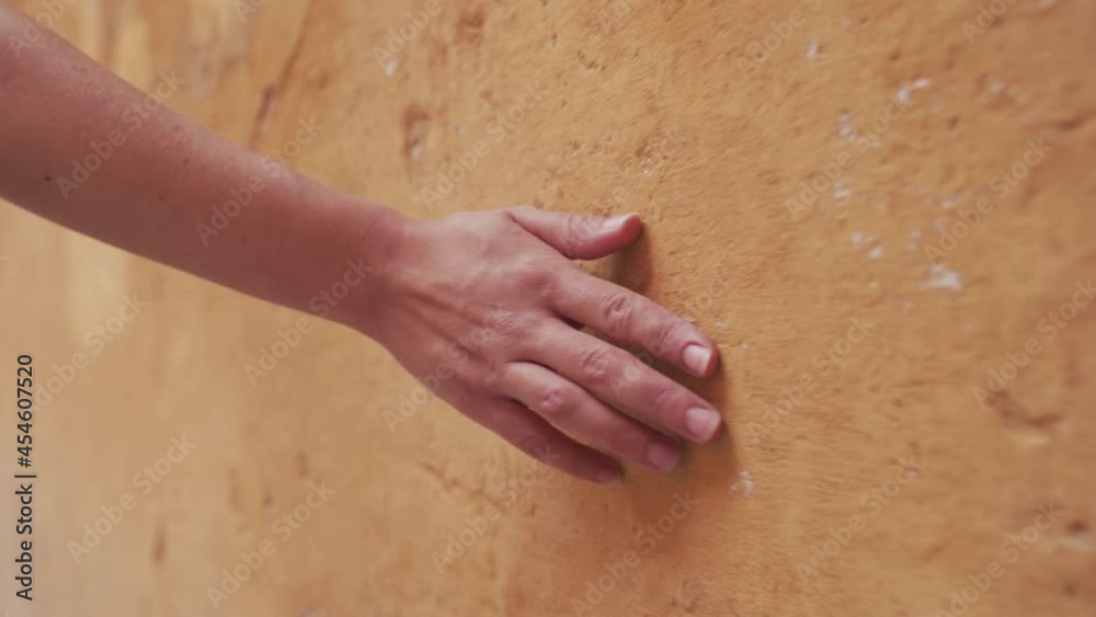 Mano deslizándose por una pared de color naranja o albero