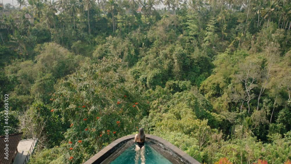 aerial view travel woman swimming in infinity pool at tropical hotel spa with view of jungle enjoying luxury lifestyle on exotic summer vacation 4k