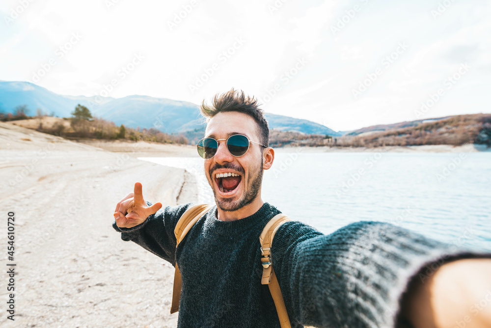 Handsome man with backpack taking selfie outdoor - Young hiker travel on mountains smiling at camera - Travel, technology and lifestyle concept