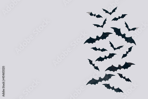 Halloween background - decorative black paper bats on light gray background with copy space for text. Halloween decorations or party invitation concept. Selective focus