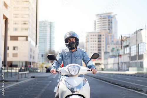 Middle shot of a young motorcyclist stopped at a traffic light in Barcelona. The man rides through the city on his white scooter on a big avenue full of skyscrapers. photo