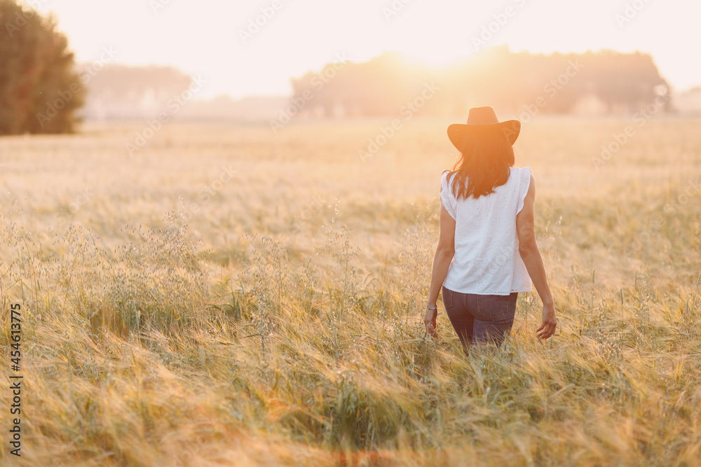 Woman farmer in cowboy hat walking at agricultural field on sunset. Labor day concept Woman farmer in cowboy hat walking at agricultural field on sunset. Labor day concept
