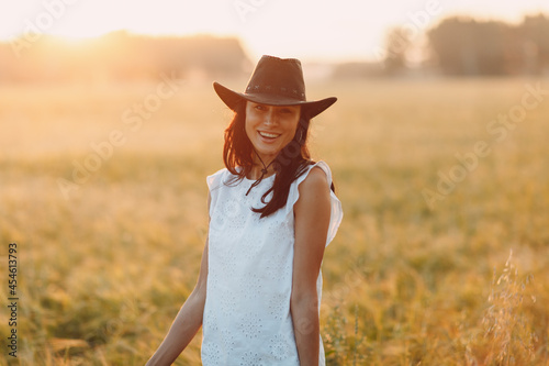 Woman farmer in cowboy hat at agricultural field on sunset.