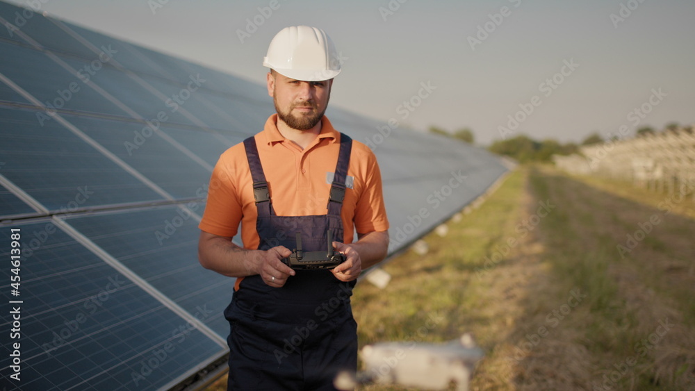 Industrial expert wearing helmet and controlling drone in photovoltaic solar power plant. Solar panel array installation. Technologies and ecology. New technologies