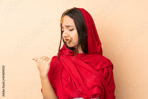 Young Indian woman isolated on beige background unhappy and pointing to the side © luismolinero