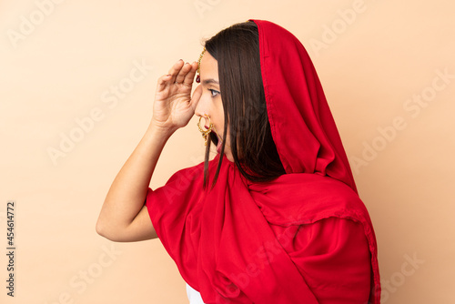 Young Indian woman isolated on beige background with surprise expression while looking side