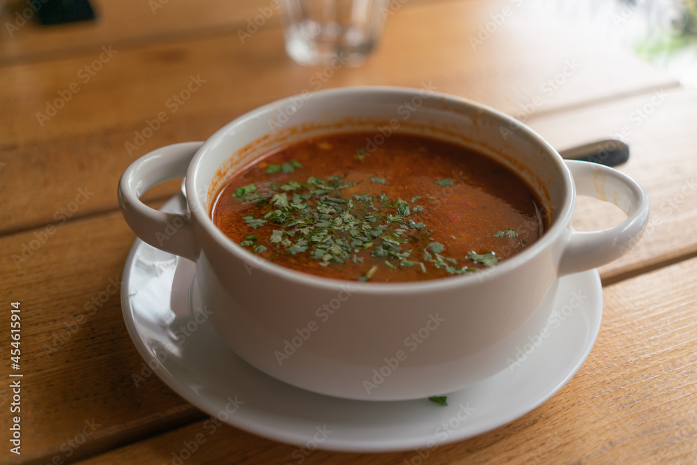 Kharcho soup with parsley in a white bowl on a wooden table in a restaurant Kharcho soup with parsley in a white bowl on a wooden table in a restaurant