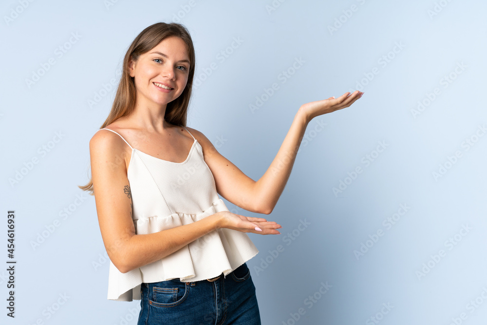 Young Lithuanian woman isolated on blue background extending hands to the side for inviting to come Young Lithuanian woman isolated on blue background extending hands to the side for inviting to come