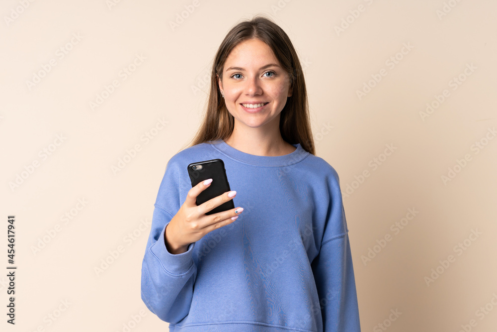 Young Lithuanian woman using mobile phone isolated on beige background smiling a lot Young Lithuanian woman using mobile phone isolated on beige background smiling a lot