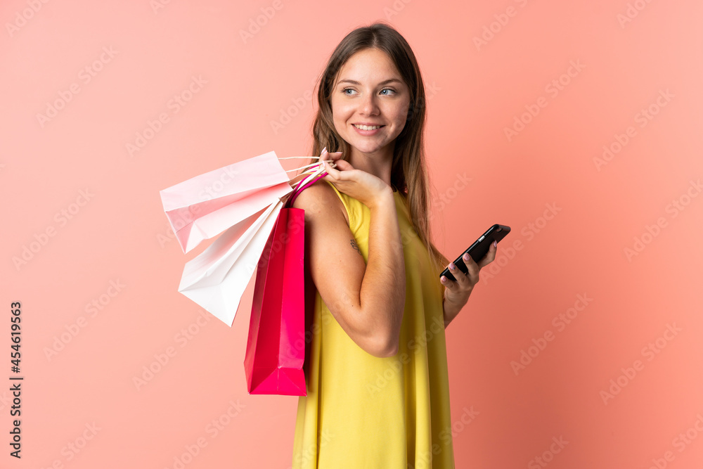 Young Lithuanian woman isolated on pink background holding shopping bags and a mobile phone
