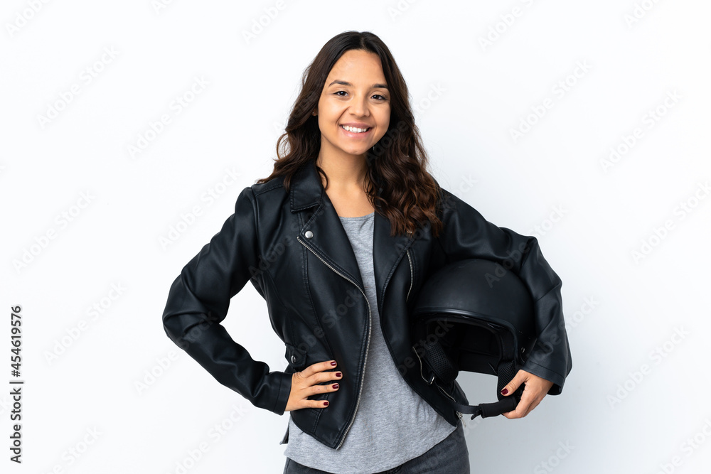 Young woman holding a motorcycle helmet over isolated white background posing with arms at hip and smiling Young woman holding a motorcycle helmet over isolated white background posing with arms at hip and smiling
