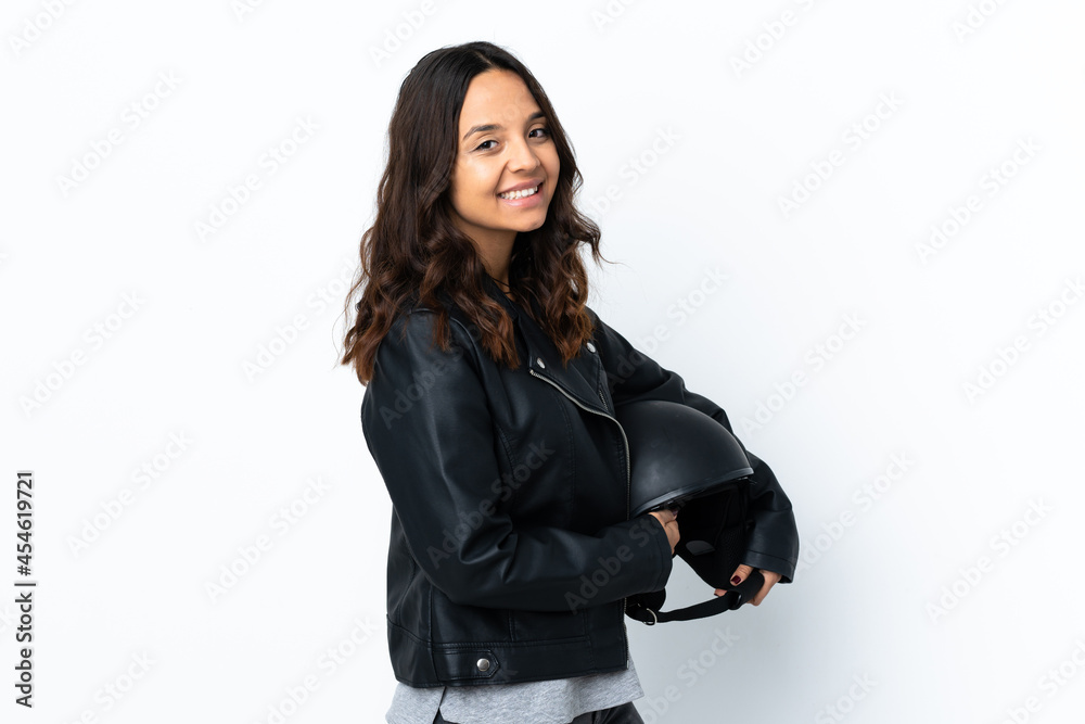 Young woman holding a motorcycle helmet over isolated white background with arms crossed and looking forward Young woman holding a motorcycle helmet over isolated white background with arms crossed and looking forward