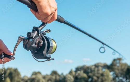 Men hands holding fishing rod or angler over blue clear sky.