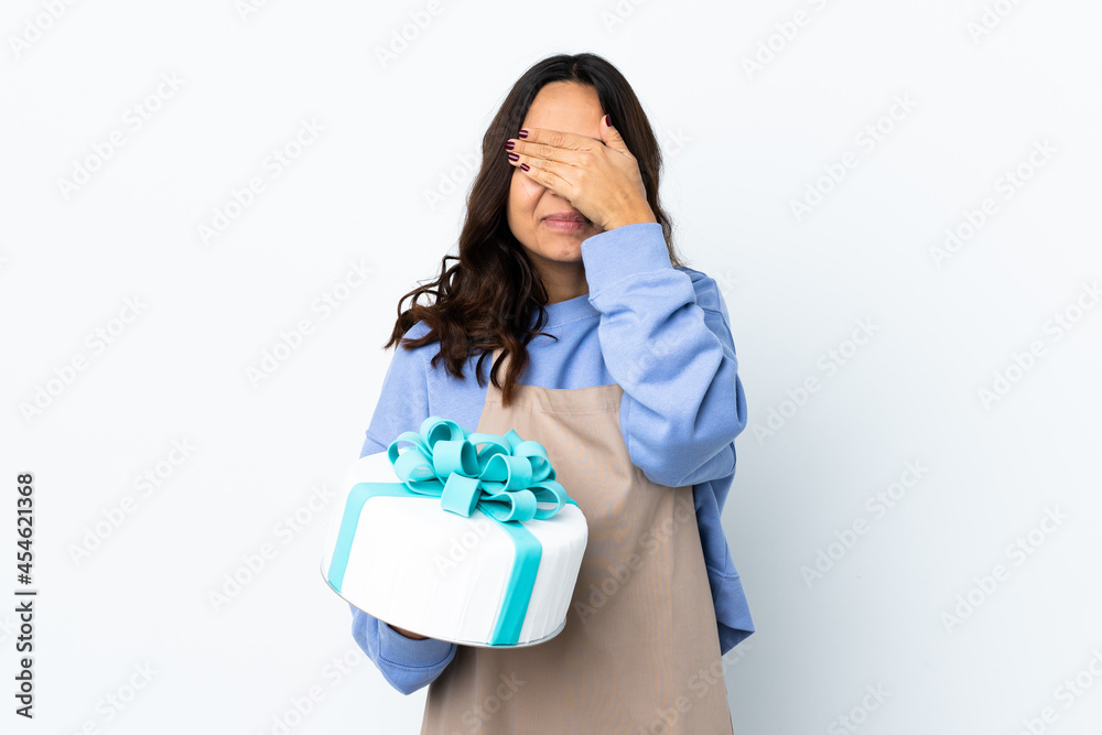 Pastry chef holding a big cake over isolated white background covering eyes by hands Pastry chef holding a big cake over isolated white background covering eyes by hands