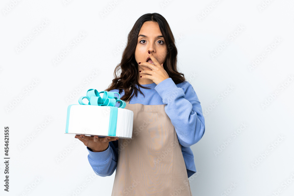Pastry chef holding a big cake over isolated white background surprised and shocked while looking right Pastry chef holding a big cake over isolated white background surprised and shocked while looking right