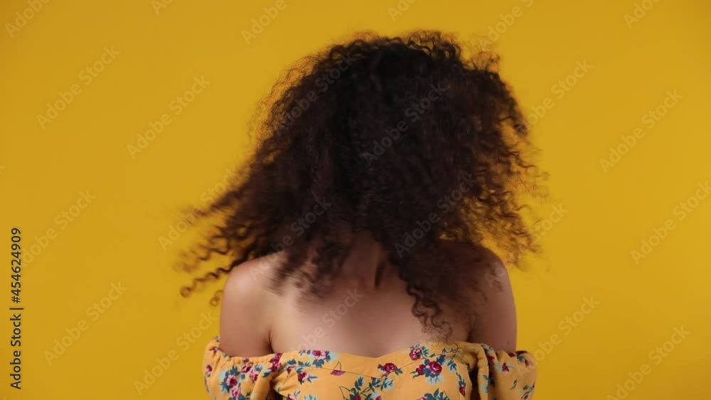 Magnificent overjoyed excited jubilant happy young latin curly woman 20s wears casual flower dress dance waving fooling around have fun enjoy play fluttering hair isolated on plain yellow background