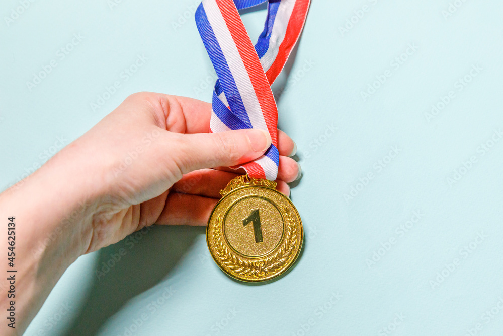 Simply flat lay design hand holding winner or champion gold trophy medal isolated on blue colorful background. Victory first place of competition. Winning or success concept. Top view copy space. Simply flat lay design hand holding winner or champion gold trophy medal isolated on blue colorful background. Victory first place of competition. Winning or success concept. Top view copy space.