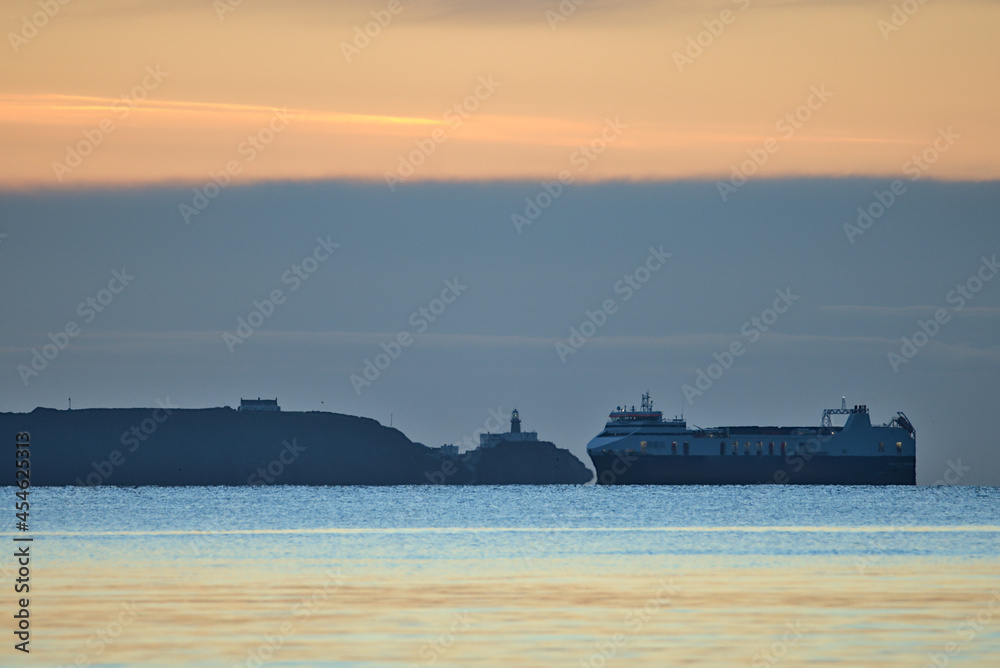Beautiful early morning view of sea truck ferry ship in Irish Sea near Baily lighthouse seen from Blackrock Beach, Dublin, Ireland. Soft and selective focus. Sunrise marine themed