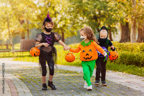 Three running kid with a basket for sweets wearing face mask on Halloween holiday