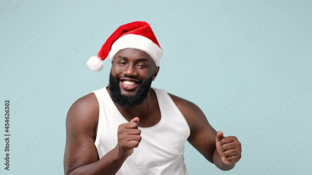 Merry young african american Santa man in white tank top Christmas hat dance wave rise expressive gesticulating hands have fun enjoy celebrate isolated on plain light blue background studio portrait Merry young african american Santa man in white tank top Christmas hat dance wave rise expressive gesticulating hands have fun enjoy celebrate isolated on plain light blue background studio portrait