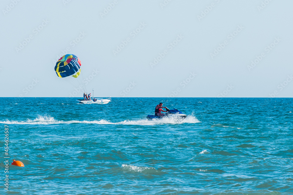 Ukraine, Iron Port - August 25, 2020: Extreme sports and exciting rest. A man rides a water bike on a blue sea against the background of the horizon line and tourists with a parashut in a motor boat