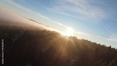 flight over the misty forest on morning with fog and sun rays on treetops at mountain sunrise. Aerial shot on fpv drone over clouds nature landscape with mountain hilly terrain. Cinematic view. photo