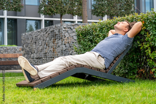 Fotografie Handsome man relaxing on wooden chaise lounge in city park