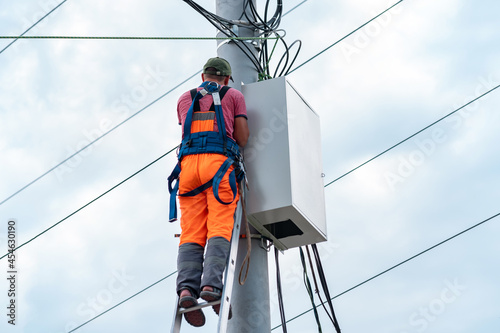 electrician or telecommunications lineman works on laying a cable at the top of a telephone pole photo