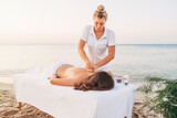 A young masseuse in white clothes makes a massage on the seashore at dawn.